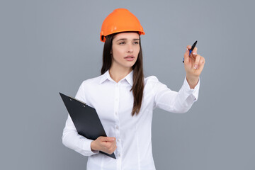 Young woman construction manager. Woman builder isolated portrait with protect helmet and clipboard. Gray background, copy space.