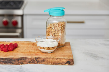 Yogurt with granola, and raspberries and strawberries next to jar with granola in a bright modern kitchen