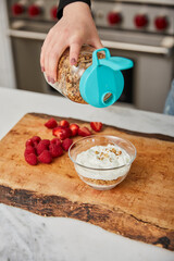 A woman topping yogurt with granola in a bright modern kitchen