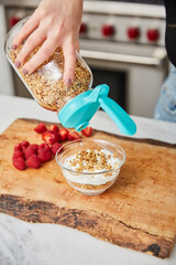A woman topping yogurt with granola in a bright modern kitchen