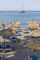 Straw umbrellas and sunbeds on a sandy beach by the sea. In the background the ship, the island. Beautiful sunny day on the Spanish coast, Europe.