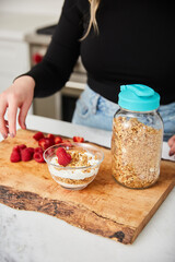 A woman topping yogurt and granola with fruit in a bright modern kitchen