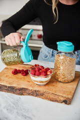 A woman topping yogurt, granola, fruit bowl with pumpkin seeds in a bright modern kitchen