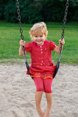 Smiling child sitting on swing. Happy kid playing in park. Girl swinging at playground in summer.