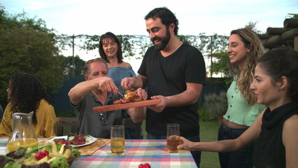 Barbecue chef bringing food to friends and family gathered around table. BBQ chef serving food to father