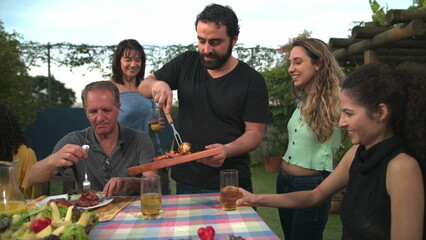 Barbecue chef bringing food to friends and family gathered around table. BBQ chef serving food to father