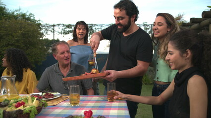 Barbecue chef bringing food to friends and family gathered around table. BBQ chef serving food to father