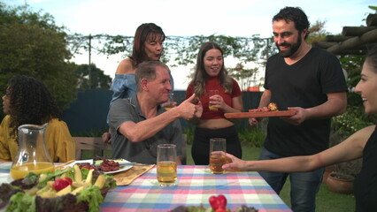 Barbecue chef bringing food to friends and family gathered around table. BBQ chef serving food to father