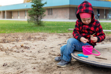 Small child playing with sand and toys outdoors at school yard on sunny day. Little girl sitting at playground