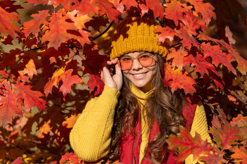 positive child in sunglasses at autumn leaves on natural background