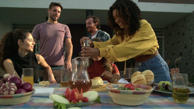 Friends gathered for backyard barbecue. Girl adding black pepper to friends plate