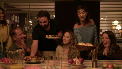 Friends and family united together around table in home backyard. People bringing food to group celebrating friendship