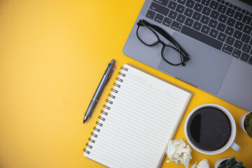 Business, technology, study, and learning concept. Copy space on office workspace yellow desk table with laptop, coffee, a pen, notebook, plant. flat lay equipment office on yellow background.