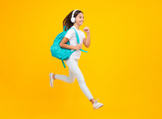 Happy teenager portrait. School girl in headphones on isolated studio background. School and music concept. Jump and run, jumping child.