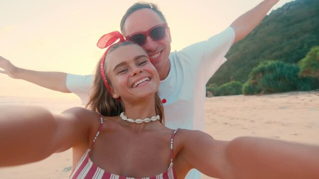 Selfie view cheerful young Caucasian man and woman rejoice at opportunity to relax and smile filming themselves on camera or make video call to friends to invite them on trip stands on sea beach
