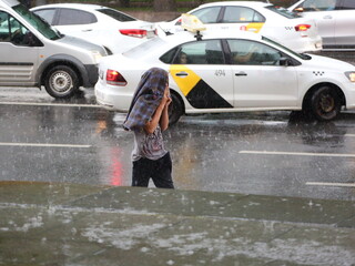 A man with a jacket on his head during heavy rain on a city street, St. Isaac's Square, St. Petersburg, Russia, July 2022