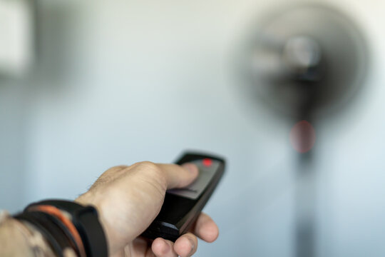 Person turning on a fan in the middle of a heat wave with a remote control to receive fresh air in the room