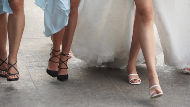 Close up of bride feet in white shoes, pretty bridemaids in pale blue dresses, high heels walking on wedding day. Woman in elegant fluttering white dress partying flexing with girlfriends. Slow motion