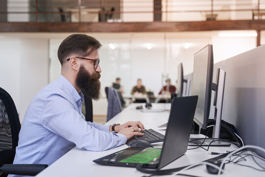 Senior computer programmer developer working in IT office, sitting at desk and coding, working on a project in software development company or startup.