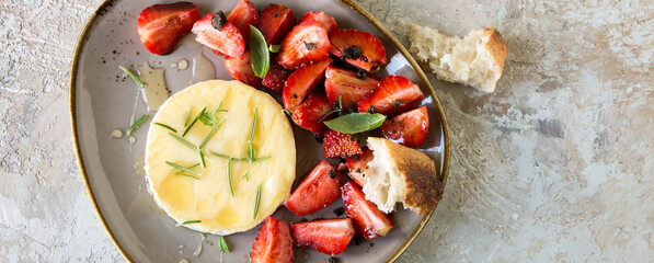 plate with baked camembert with strawberries and rosemary on a light table