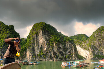 Joven fotógrafo haciendo fotos desde una barca típica en Halong Bay, Vietnam