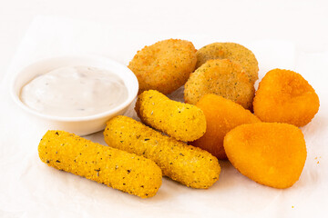 Selection of breaded fried cheese on a white baking paper with white dip.