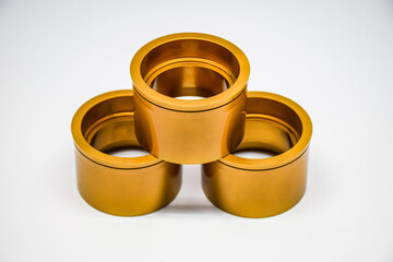 Three large perforated metal cylindrical tubes pierced through dark gold like gold and brass with curved slits overlaid on a white background.