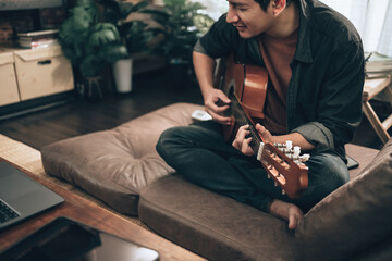 young man relax and playing guitar while sitting on sofa bed in living room at home. Music hobby...