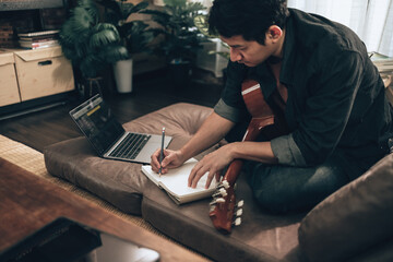 young man relax and playing guitar while sitting on sofa bed in living room at home. Music create...