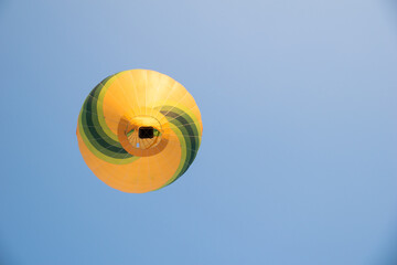 Hot air balloon with summer colors like green and yellow seen from the ground with the blue sky in the background.
image with space for text.