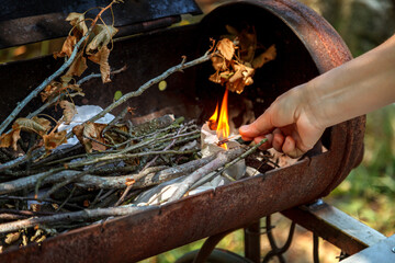 A womans hand burns paper in a barbecue with a burning match