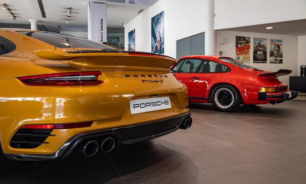 Matosinhos, Portugal - June 25, 2022: A picture of an orange Porsche 911 Turbo S next to a red Porsche 911 Carrera 3.0 inside a dealership.