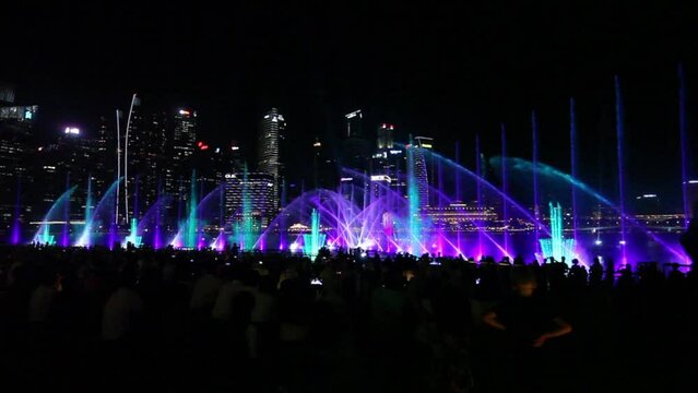 Water and laser light show of fountains in Singapore. A beautiful evening show for visiting tourists in city main square. Night city and many travelers watching the amazing performance. Asia travel