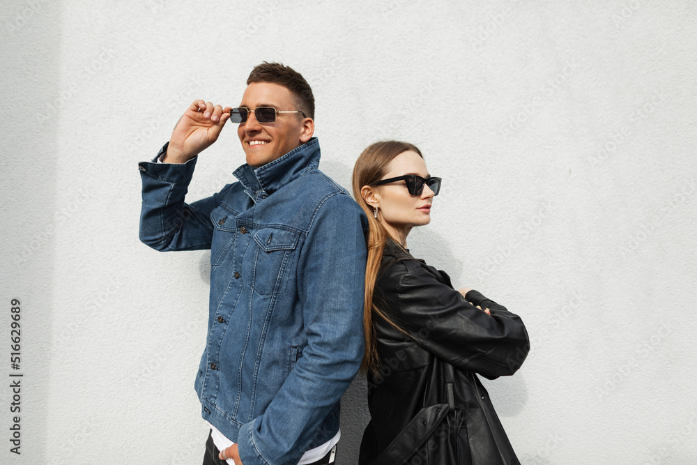 Canvas Prints Fashionable young couple in trendy urban casual clothes posing near a wall on the street. Fashion handsome happy hipster man and his girlfriend wearing vintage sunglasses in stylish denim outfit