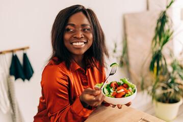 Beautiful young woman eating salad in the kitchen in the morning. Healthy food. Close up. Portrait...