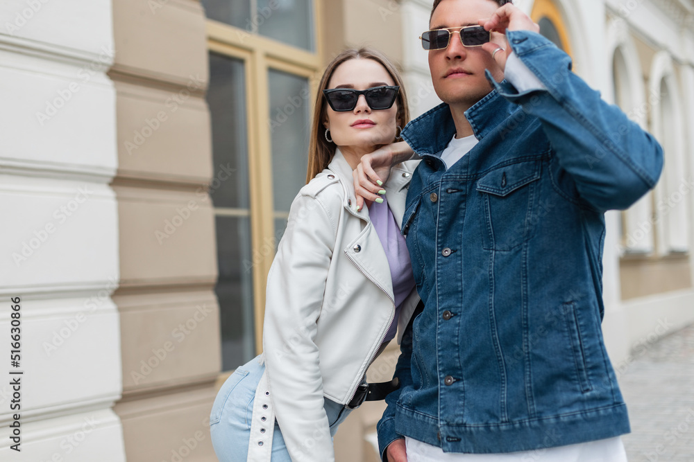 Wall mural Fashionable beautiful young couple woman and man hipster with vintage sunglasses wearing trendy casual denim with denim jacket and stylish leather jacket are walking in the city