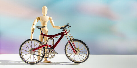 wooden mannequin in form of man near metal model of bicycle. male cyclist stands next to his bike against blurred background of clouds at sunset