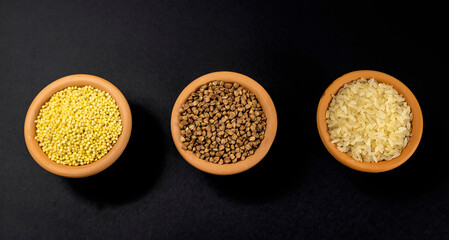 A set of cereals for preparing porridge for breakfast. Cereals in clay bowls: millet, rice, buckwheat on a black background.