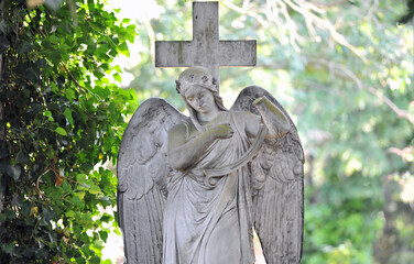 An old, weathered sandstone sculpture of a grieving angel on a cemetery in Berlin Germany.