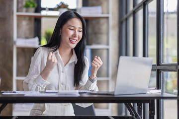 Fototapeta premium Happy excited Asian businesswoman in the office working with a laptop computer, Yes great job.