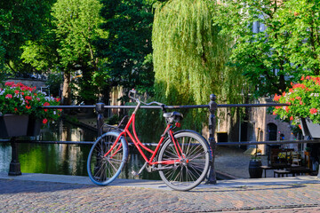 Red bicycle locked and parked on a bridge placed over Oudegracht canal in Utrecht.
