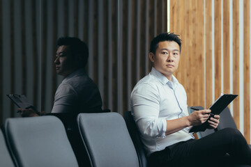 A man is waiting for an interview in the corridor of an office center, an Asian businessman is looking for a job