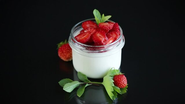 Sweet homemade yogurt with fresh ripe strawberries in a glass jar isolated on black background