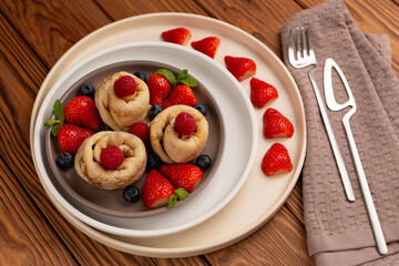 delicious thin pancakes in the shape of barrels on three plates with fresh raspberries, strawberries and blueberries on a wooden table