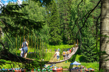 People cross the suspension bridge over the Chusovaya River. Parking of colorful boats and...