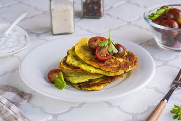 Zucchini fritters on a white plate on a light tiled concrete background. Zucchini or squash recipes. Vegetarian recipes.