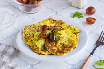 Zucchini fritters on a white plate on a light tiled concrete background. Zucchini or squash recipes. Vegetarian recipes.