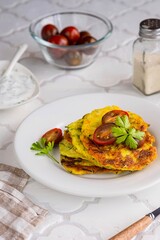 Zucchini fritters on a white plate on a light tiled concrete background. Zucchini or squash recipes. Vegetarian recipes.