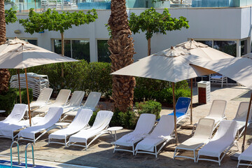 Umbrellas and beach chairs (sun bed) around outdoor swimming pool with date palms trees for...