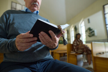 Hands of senior male parishioner of Catholic church holding open Holy Bible in black leather cover...